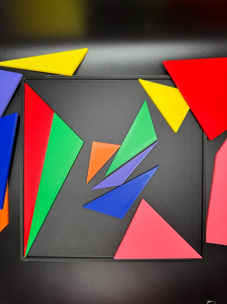 May include: A set of colorful geometric shapes, including red, green, blue, purple, orange, and yellow, arranged on a black surface. The shapes are all triangles and are arranged in a pattern.