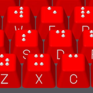 May include: Red keyboard with white keys and braille dots on each key. The keys are labeled with letters of the alphabet.