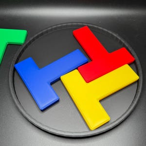 Op de afbeelding: Vier kleurrijke puzzelstukken, rood, geel, blauw en groen, zijn in een cirkel op een zwarte achtergrond gerangschikt. De stukken zijn L-vormig en passen in elkaar om een ​​grotere vorm te vormen.