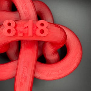 May include: A red 3D printed object shaped like a knot with the numbers "8-18" printed on it.
