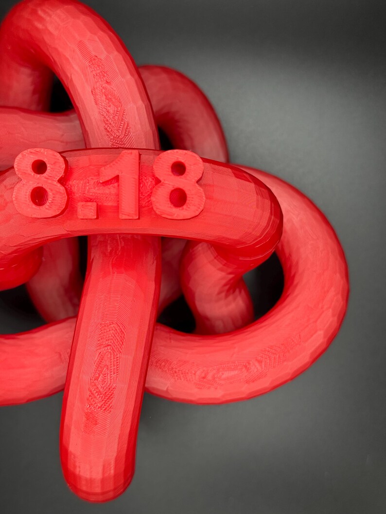 May include: A red 3D printed object shaped like a knot with the numbers "8-18" printed on it.