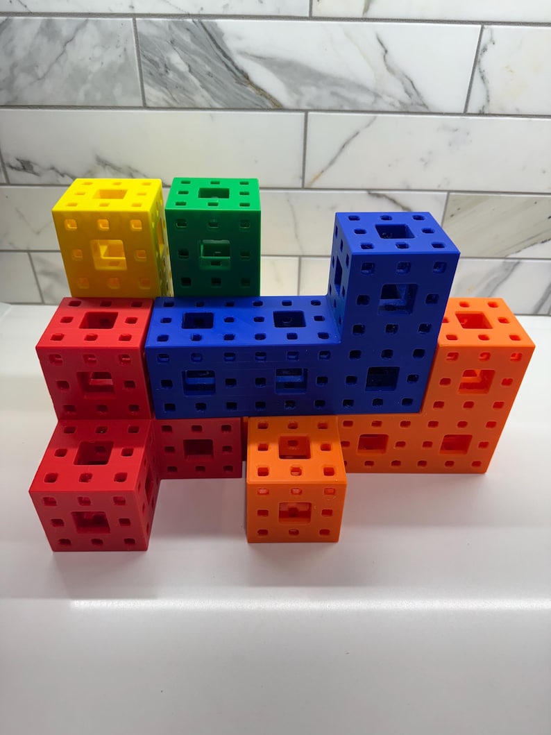 May include: A set of colorful building blocks in red, orange, yellow, green, and blue. The blocks are made of plastic and have a grid pattern on each side. They are arranged in a tower-like structure.