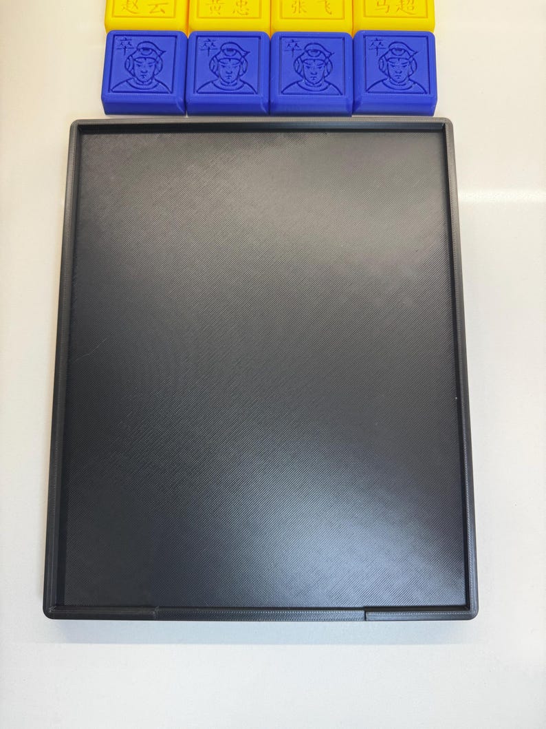 May include: A black rectangular tray with a smooth, textured surface. The tray is made of plastic and has a slightly raised edge.