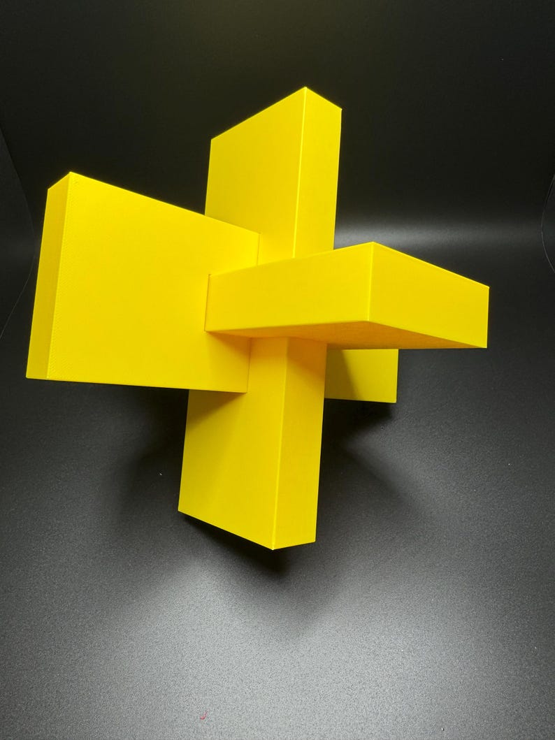 K&ouml;nnte beinhalten: Eine gelbe geometrische Skulptur aus vier sich schneidenden rechteckigen Prismen.
