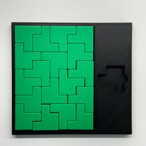 May include: A green and black puzzle game with a square grid of green puzzle pieces and a black frame. The puzzle pieces are shaped like L's and fit together to form a larger shape. The black frame has a cutout in the shape of a T.