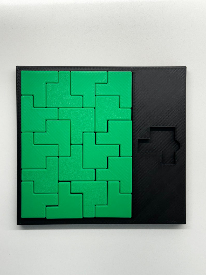 May include: A green and black puzzle game with a square grid of green puzzle pieces and a black frame. The puzzle pieces are shaped like L's and fit together to form a larger shape. The black frame has a cutout in the shape of a T.