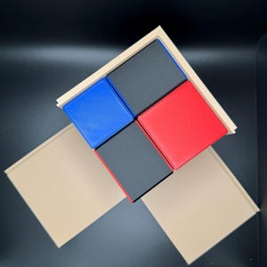 May include: Four square blocks in a wooden frame. The blocks are black, red, blue, and black. The frame is a light brown color.