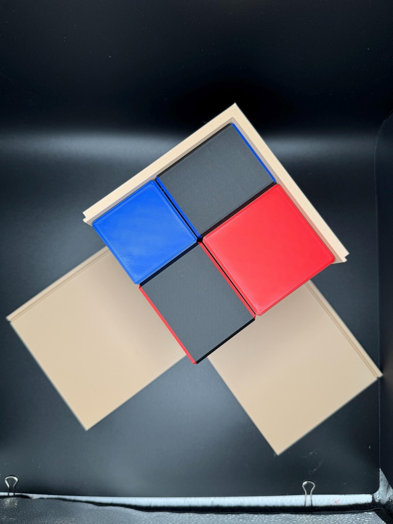 May include: Four square blocks in a wooden frame. The blocks are black, red, blue, and black. The frame is a light brown color.
