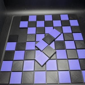 Puede incluir: Un juego de tablero de ajedrez negro y morado con fichas cuadradas individuales. El tablero es negro con cuadrados negros y morados alternados. Algunas fichas est&aacute;n apiladas encima del tablero.