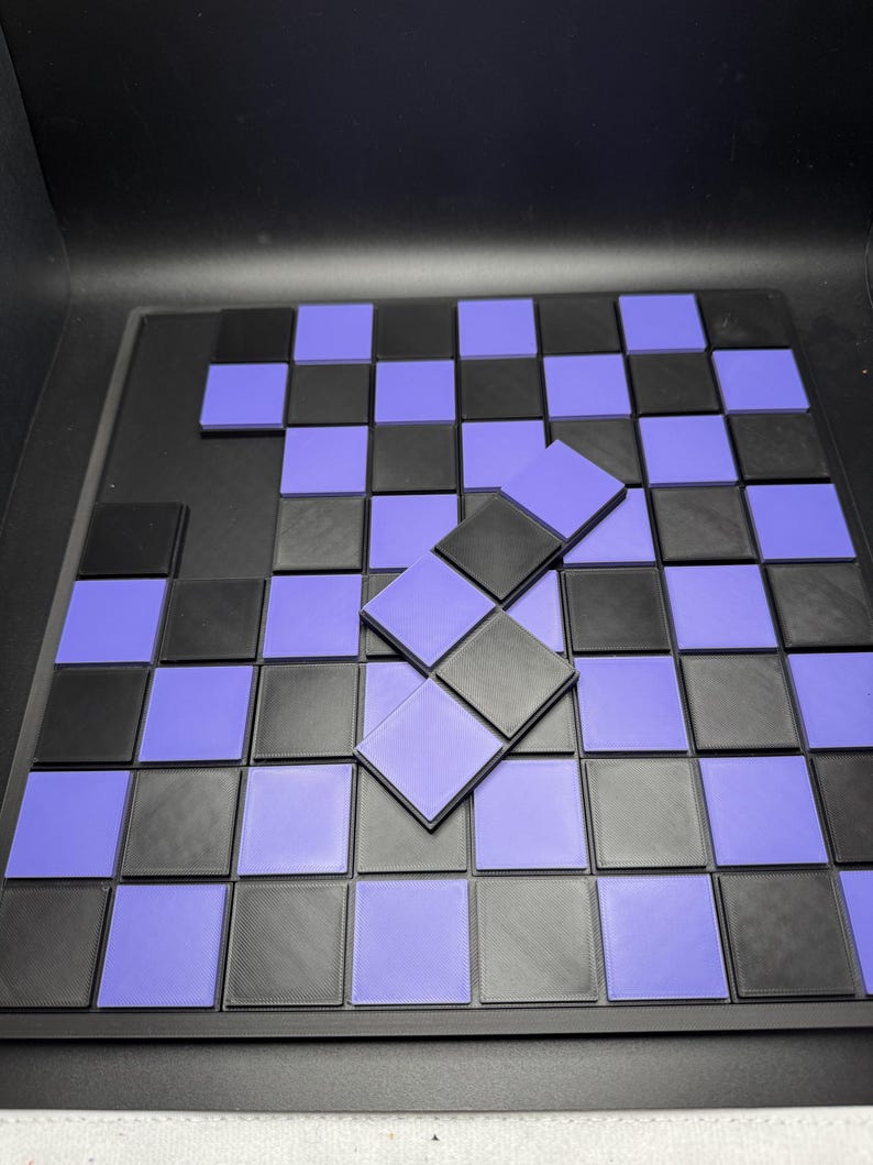 Puede incluir: Un juego de tablero de ajedrez negro y morado con fichas cuadradas individuales. El tablero es negro con cuadrados negros y morados alternados. Algunas fichas est&aacute;n apiladas encima del tablero.