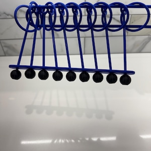 Pode incluir: Um ber&ccedil;o de Newton de metal azul com dez bolas pretas suspensas em uma moldura. As bolas est&atilde;o alinhadas em uma fila e todas s&atilde;o do mesmo tamanho.