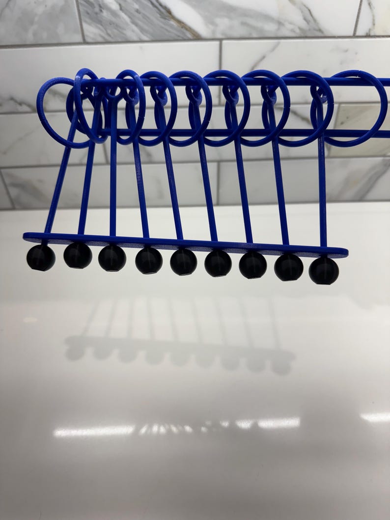 Pode incluir: Um ber&ccedil;o de Newton de metal azul com dez bolas pretas suspensas em uma moldura. As bolas est&atilde;o alinhadas em uma fila e todas s&atilde;o do mesmo tamanho.