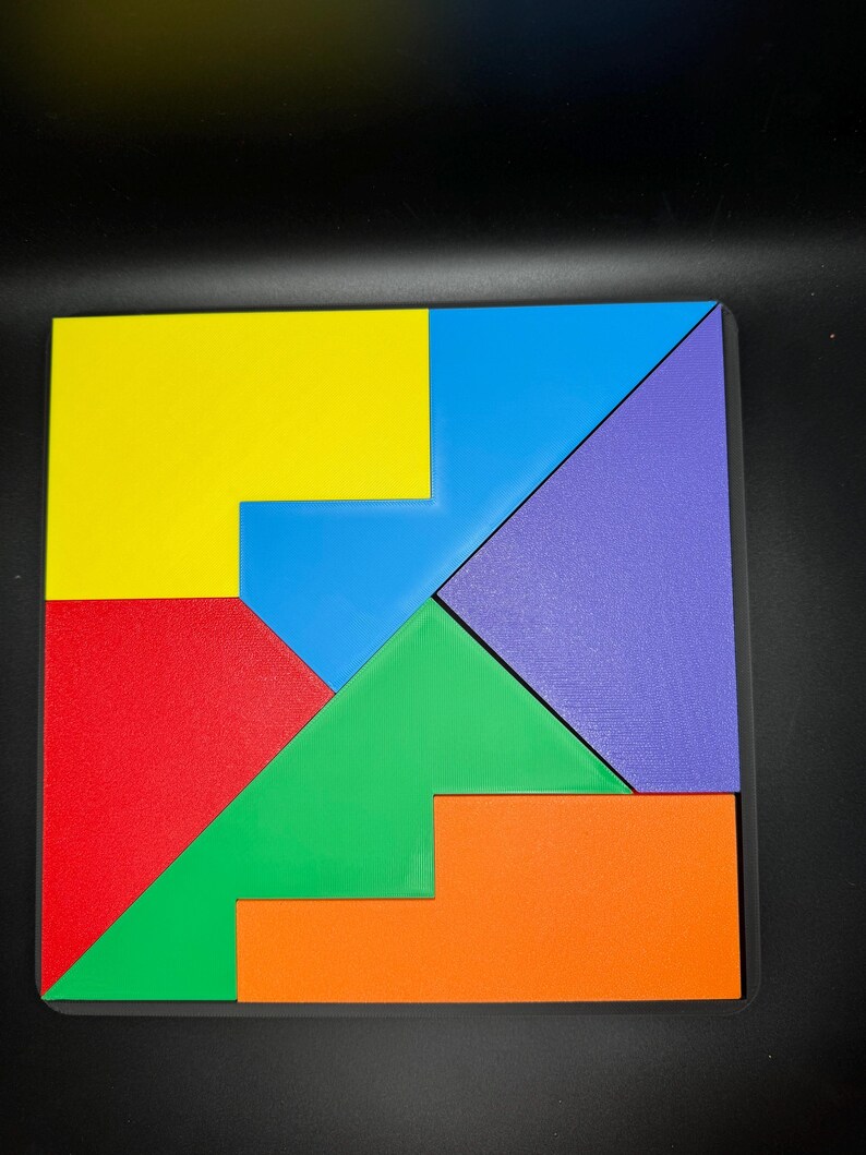 May include: A colorful tangram puzzle with seven pieces in yellow, blue, green, red, purple, and orange. The pieces are arranged to form a square.