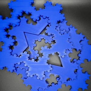 May include: A close-up of a pile of blue 3D printed snowflake ornaments. The snowflakes are layered on top of each other, creating a unique and intricate design.