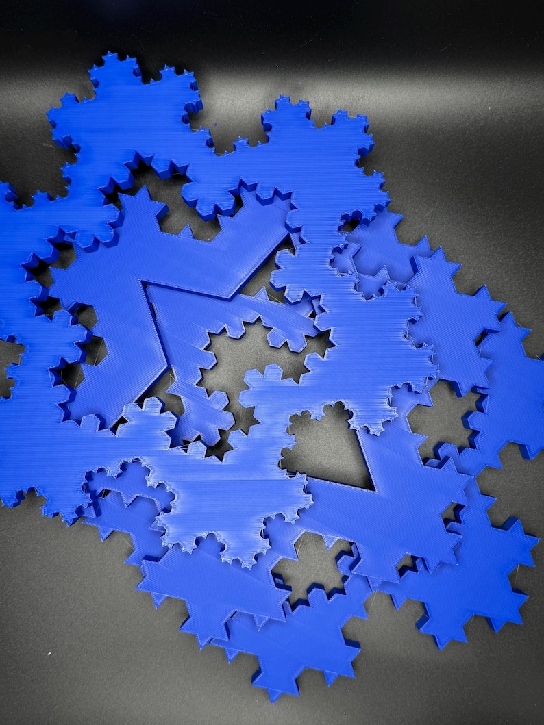 May include: A close-up of a pile of blue 3D printed snowflake ornaments. The snowflakes are layered on top of each other, creating a unique and intricate design.