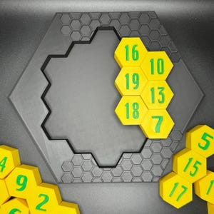 Puede incluir: Un juego de rompecabezas hexagonal con fichas hexagonales amarillas numeradas del 4 al 20. Las fichas est&aacute;n dispuestas en un patr&oacute;n de panal en un tablero hexagonal negro.