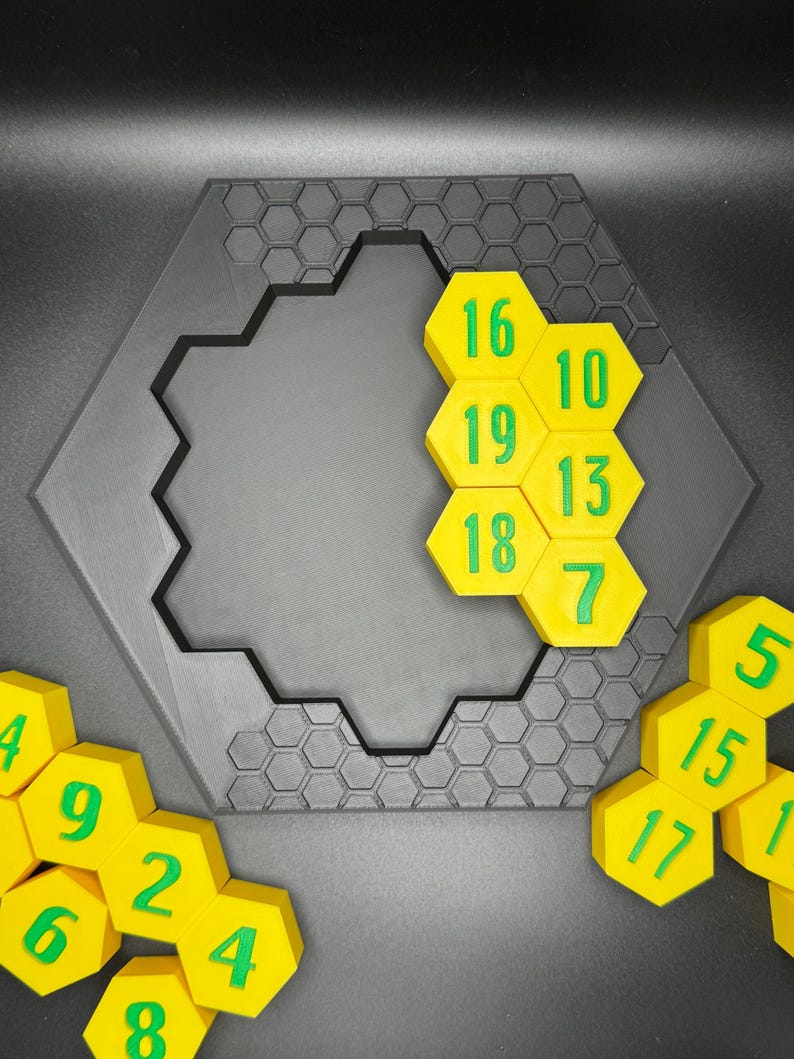 Puede incluir: Un juego de rompecabezas hexagonal con fichas hexagonales amarillas numeradas del 4 al 20. Las fichas est&aacute;n dispuestas en un patr&oacute;n de panal en un tablero hexagonal negro.