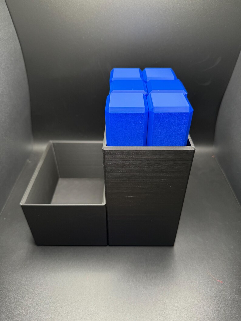 May include: A black 3D printed organizer with a rectangular compartment and a square compartment. The square compartment holds six blue rectangular blocks.