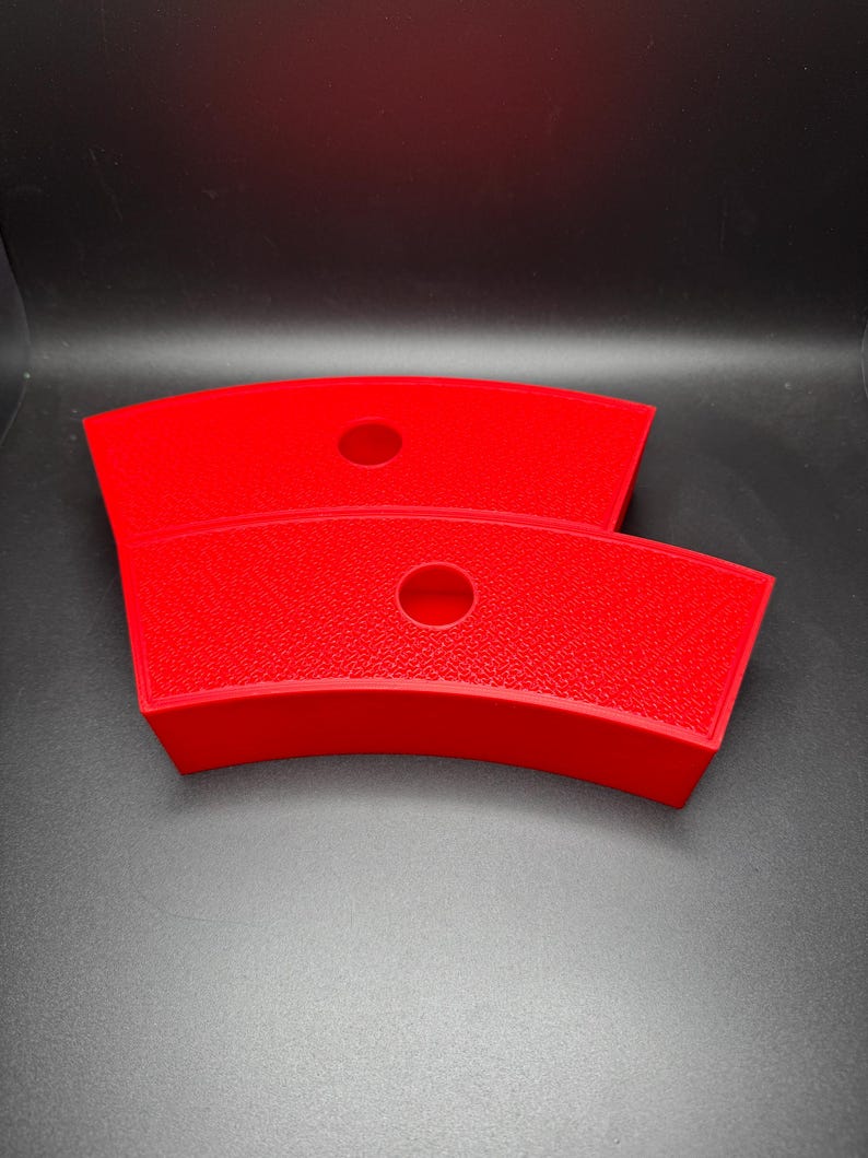 May include: Two bright red, curved plastic trays with a textured surface. Each tray has a circular hole in the center. The trays are stacked on top of each other against a dark background.