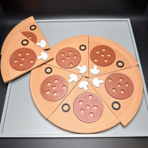 May include: A toy pizza set made of light tan dough-colored material, featuring several triangular slices. Each slice is topped with a brown pepperoni circle with six holes, a small white mushroom piece, and a thin black olive ring.