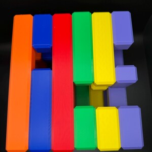 May include: A colorful wooden puzzle with six pieces in orange, blue, red, green, yellow, and purple. The pieces are arranged in a stack, with the top piece being purple.