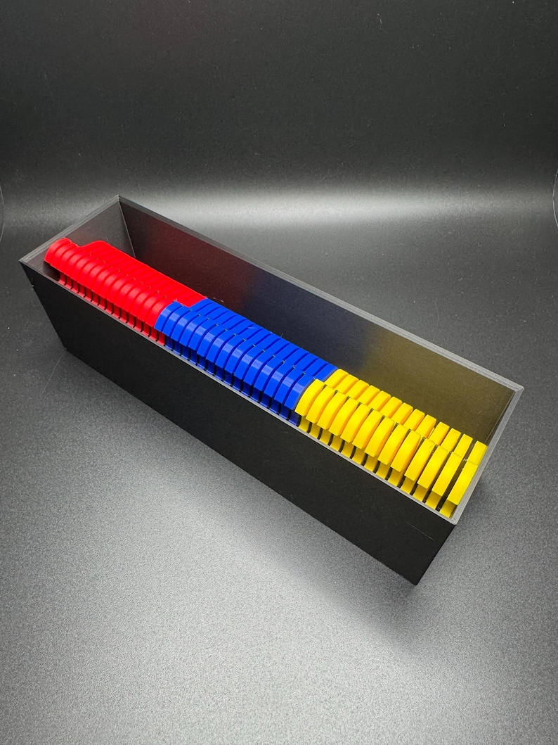 May include: A black rectangular container filled with colorful plastic pieces. The pieces are stacked in three rows, with red on the bottom, blue in the middle, and yellow on top.