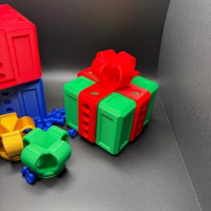 May include: A green gift box with a red bow and red ribbon. The box has a series of holes on the sides. The box is sitting on a gray surface.