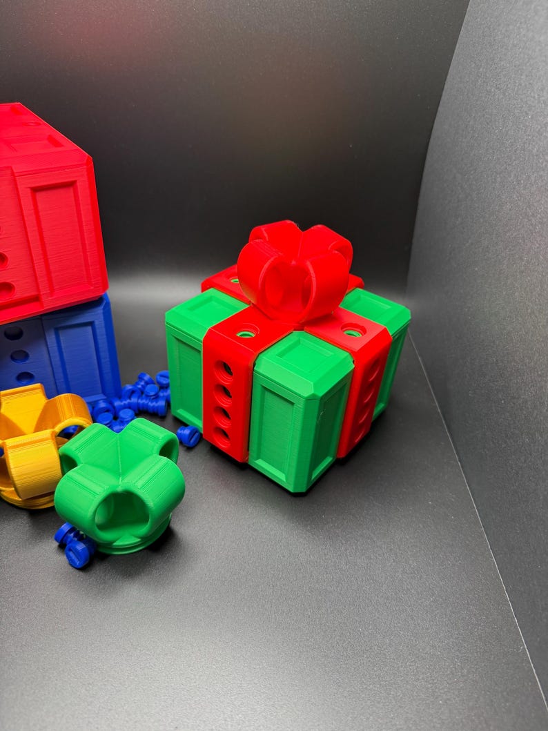 May include: A green gift box with a red bow and red ribbon. The box has a series of holes on the sides. The box is sitting on a gray surface.