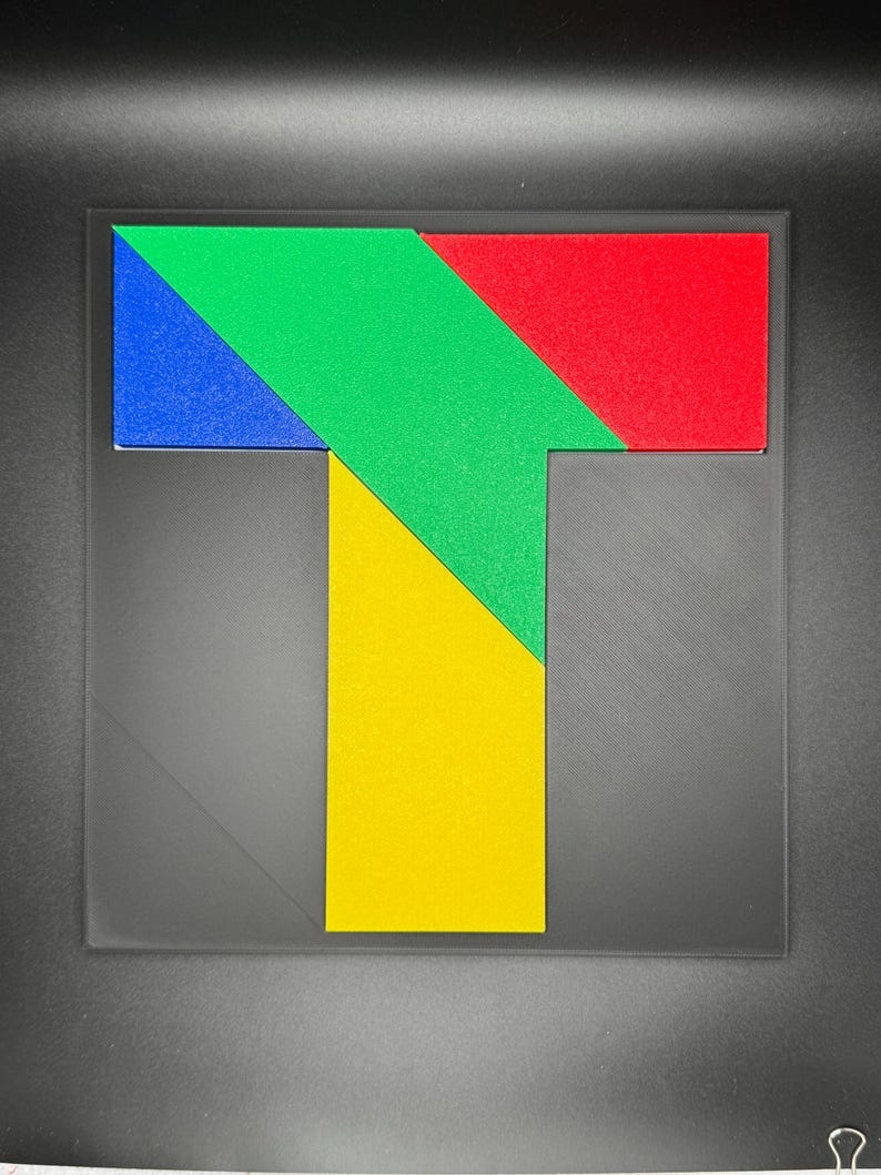 May include: A colorful puzzle shaped like the letter T. The puzzle is made up of four pieces: a red piece, a green piece, a yellow piece, and a blue piece.