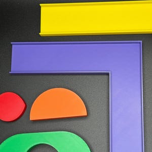 May include: A set of colorful plastic track pieces for a toy race car track. The pieces include a straight track, a curved track, and a corner track. The track pieces are yellow, purple, orange, green, and blue.