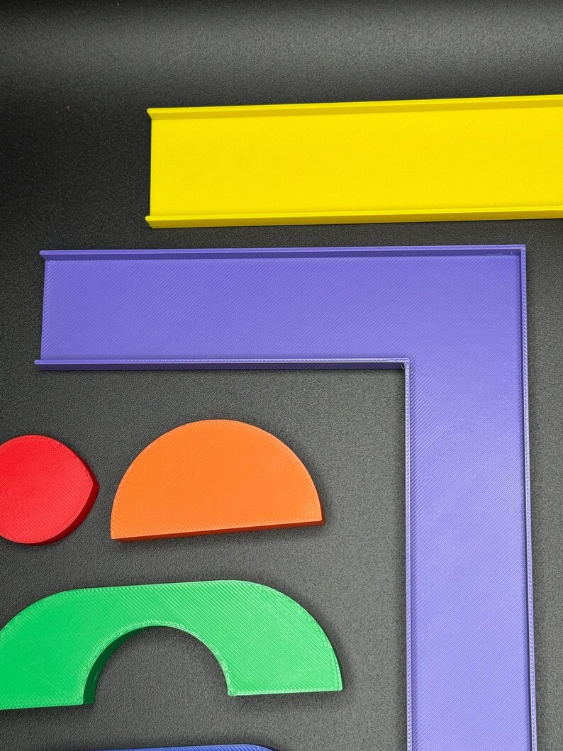 May include: A set of colorful plastic track pieces for a toy race car track. The pieces include a straight track, a curved track, and a corner track. The track pieces are yellow, purple, orange, green, and blue.
