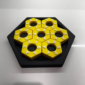 May include: A yellow hexagonal puzzle with numbers 1 through 6 on each piece. The puzzle is made of plastic and has a black base.