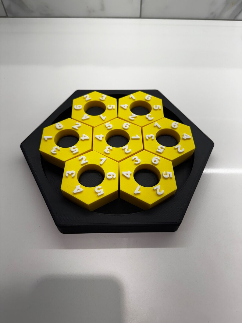 May include: A yellow hexagonal puzzle with numbers 1 through 6 on each piece. The puzzle is made of plastic and has a black base.