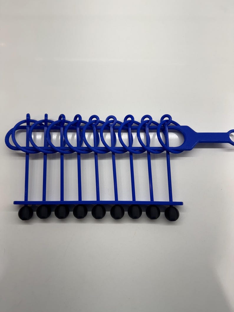 Pode incluir: Uma ferramenta de pl&aacute;stico azul com 10 pontas de borracha pretas. A ferramenta tem uma al&ccedil;a e uma s&eacute;rie de la&ccedil;os que seguram as pontas.