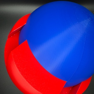 Puede incluir: Una esfera impresa en 3D con la parte superior azul y la inferior roja. La esfera est&aacute; hecha de dos mitades que encajan.