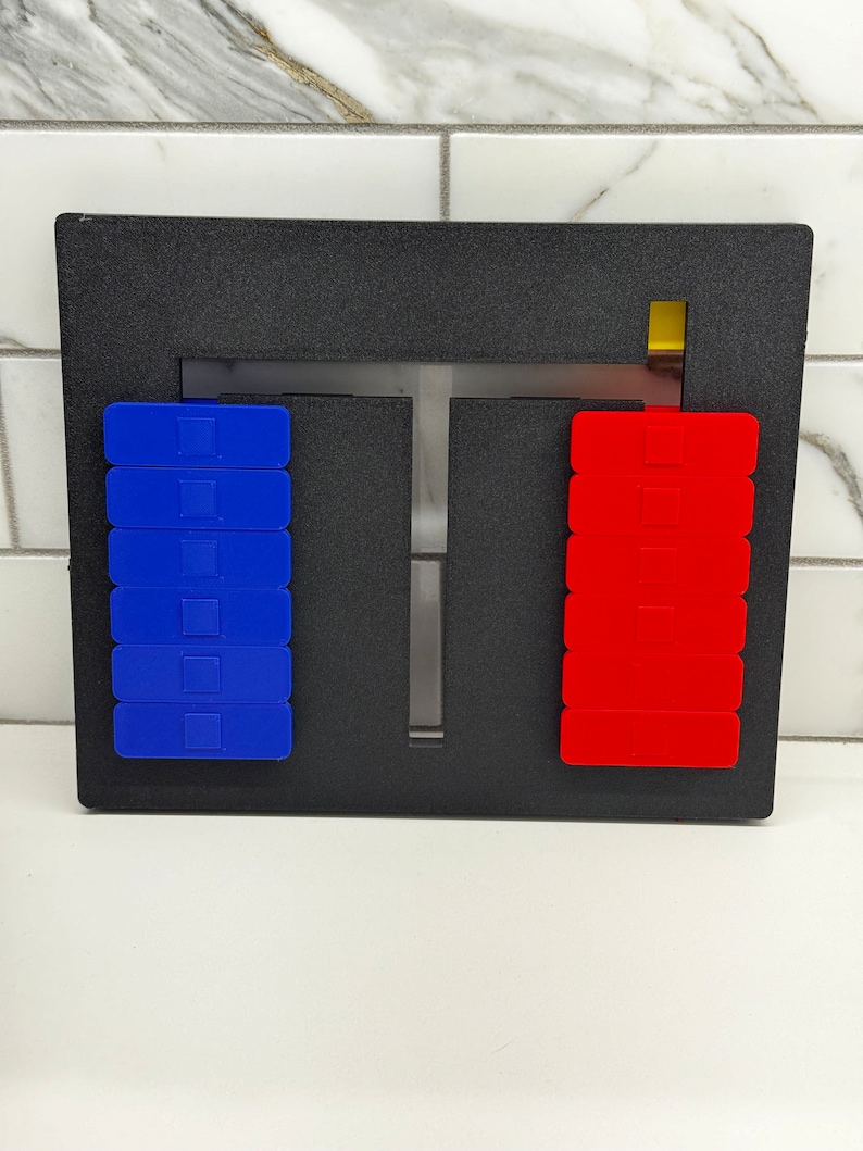 May include: A black frame with a T-shaped opening in the center. There are two stacks of blocks, one blue and one red, on either side of the opening. A small yellow block is visible at the top of the frame.