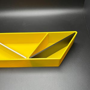 May include: A yellow triangular tray with three compartments. The tray is divided into three sections, with one section being black.
