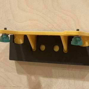 K&ouml;nnte beinhalten: Ein gelber Wandhalter mit schwarzem Sockel und zwei gr&uuml;nen Kn&ouml;pfen. Der Halter hat drei L&ouml;cher zum Aufh&auml;ngen von Gegenst&auml;nden.