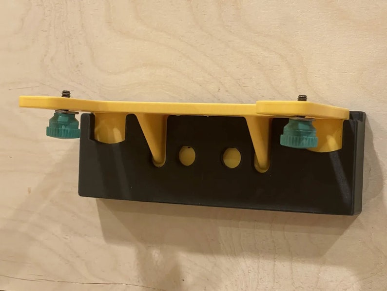 K&ouml;nnte beinhalten: Ein gelber Wandhalter mit schwarzem Sockel und zwei gr&uuml;nen Kn&ouml;pfen. Der Halter hat drei L&ouml;cher zum Aufh&auml;ngen von Gegenst&auml;nden.