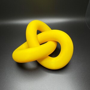 May include: A bright yellow, three-dimensional knot sculpture. The knot is made of smooth, rounded plastic and is tied in a complex pattern.