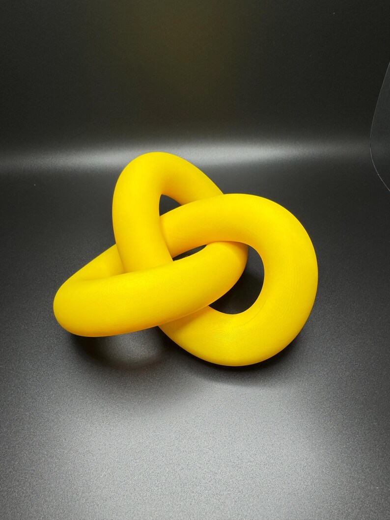 May include: A bright yellow, three-dimensional knot sculpture. The knot is made of smooth, rounded plastic and is tied in a complex pattern.