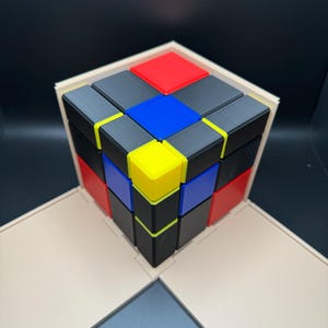 Puede incluir: Un rompecabezas de cubo 3x3 con cuadrados negros, rojos, azules y amarillos. El cubo está ensamblado en un patrón con los cuadrados de colores en el exterior.
