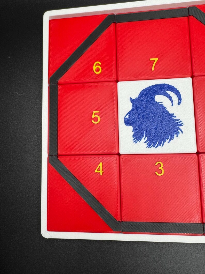 May include: A red game board with black trim and a blue goat silhouette in the center. The numbers 3, 4, 5, 6, and 7 are printed in yellow on the board.