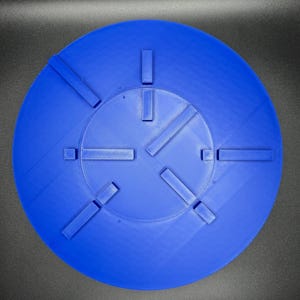 May include: A bright blue, circular object with a series of rectangular protrusions. The object has a textured surface and a central, slightly recessed area. The design features several evenly spaced, raised rectangular elements.
