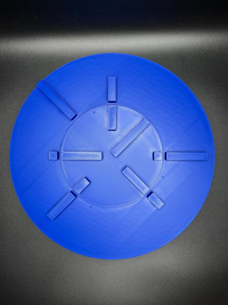 May include: A bright blue, circular object with a series of rectangular protrusions. The object has a textured surface and a central, slightly recessed area. The design features several evenly spaced, raised rectangular elements.
