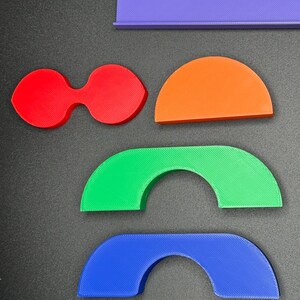 May include: A set of five colorful 3D printed shapes, including a rectangle, a teardrop shape, a half-circle, and two arches. The shapes are made of plastic and are in shades of purple, red, orange, green, and blue.