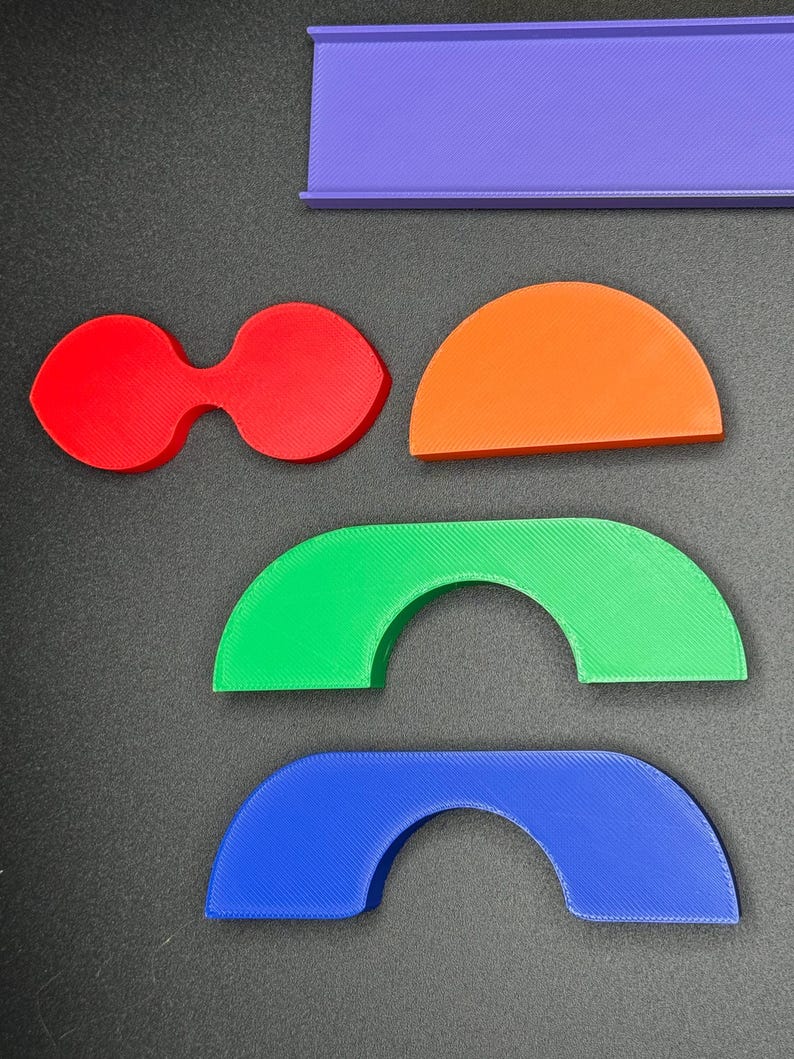 May include: A set of five colorful 3D printed shapes, including a rectangle, a teardrop shape, a half-circle, and two arches. The shapes are made of plastic and are in shades of purple, red, orange, green, and blue.