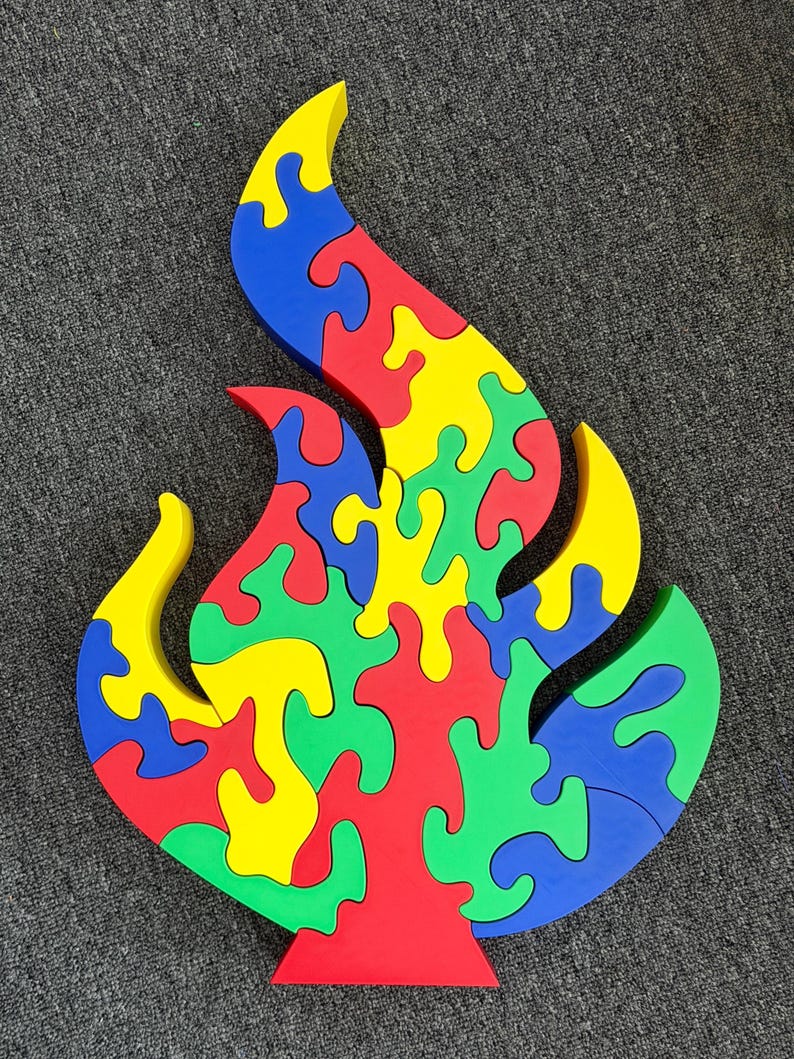 Puede incluir: Un rompecabezas de madera multicolor con forma de llama, que presenta piezas entrelazadas en tonos vibrantes de rojo, amarillo, verde y azul. El rompecabezas est&aacute; construido con segmentos gruesos de bordes lisos que encajan para formar un dise&ntilde;o de fuego.