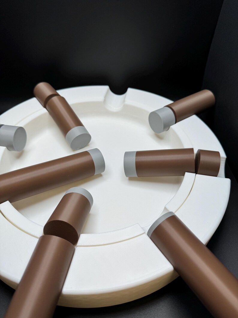 K&ouml;nnte beinhalten: Ein wei&szlig;er Aschenbecher mit kreisf&ouml;rmigem Design und mehreren braunen und grauen zigarrenf&ouml;rmigen Objekten. Der Aschenbecher hat eine glatte Oberfl&auml;che und einen gebogenen Rand. Die Zigarren sind um den Aschenbecher angeordnet.