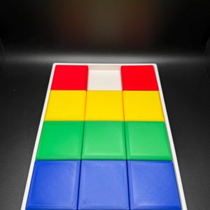 May include: A white tray with nine square blocks in four colors: red, yellow, green, and blue. The blocks are arranged in a pyramid shape, with the red blocks at the top, followed by yellow, green, and blue.